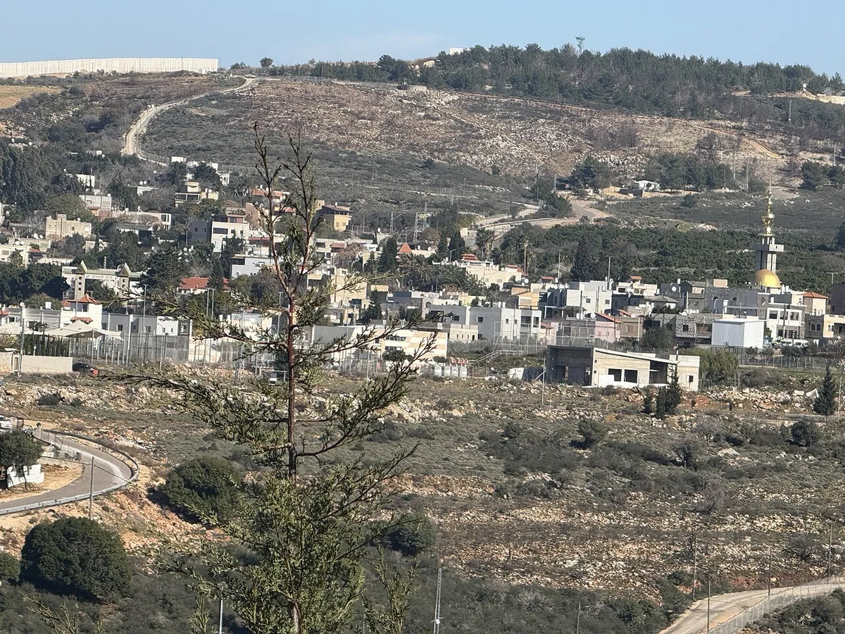 Houses and a mosque with a golden dome on a hillside, with a long wall along the ridge above