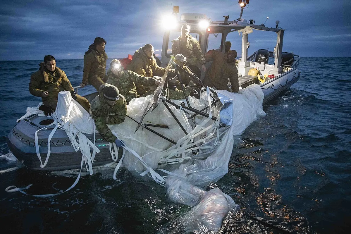 Navy sailors pulling balloon debris into a boat