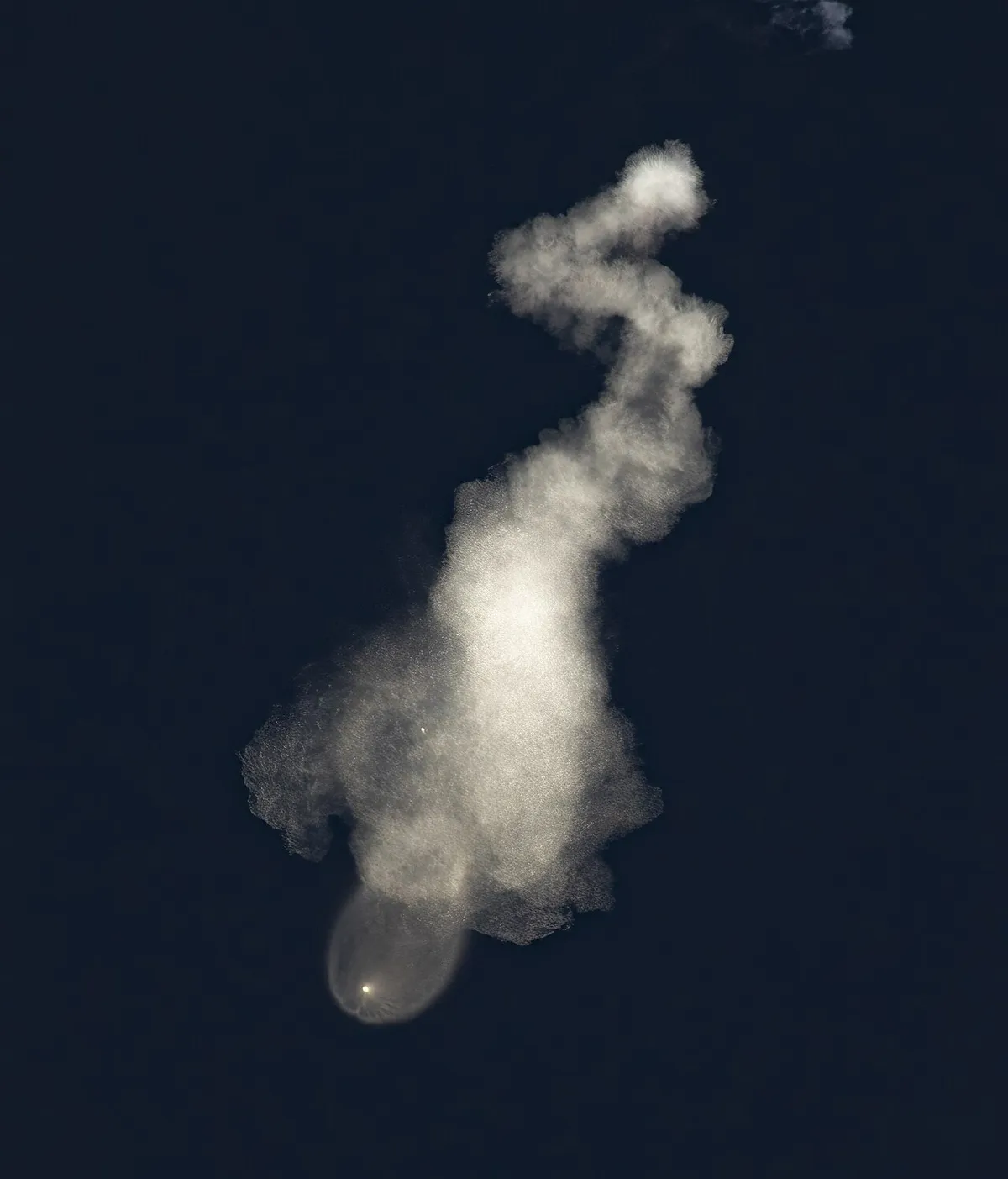 Twisting rocket exhaust trail lit by sunlight in a dark sky